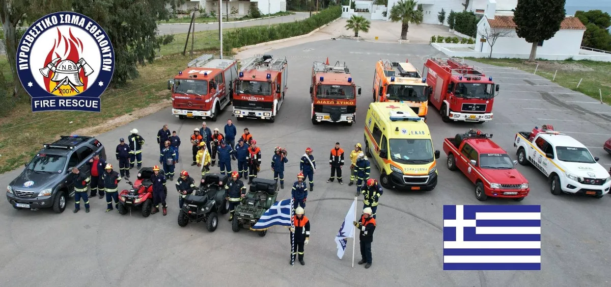 Parade mit Feuerwehrautos und Feuerwehrleuten und der griechischen Fahne.